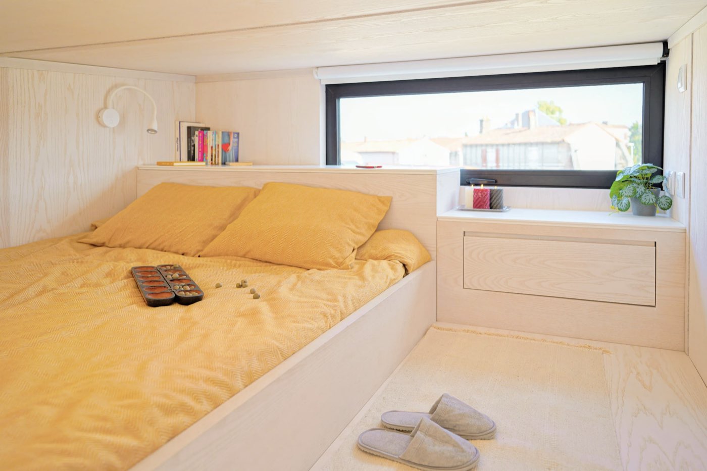 Couchage en alcôve sous la mezzanine, linge ocre et bandeau vitré