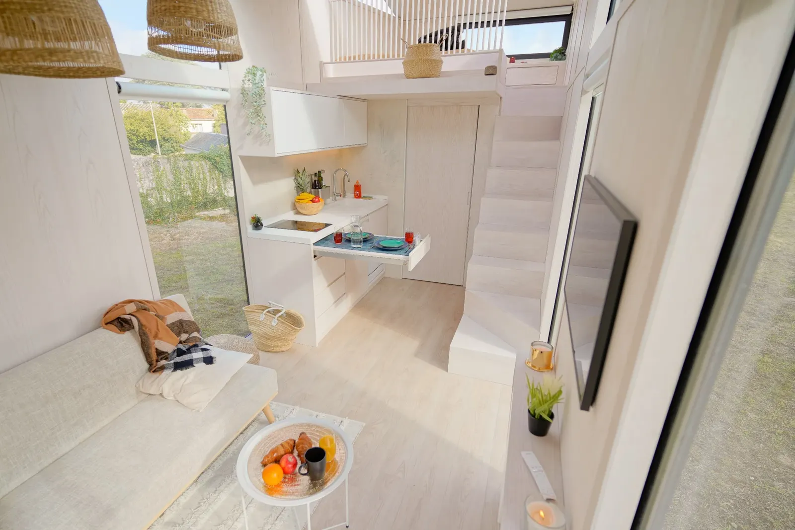 Séjour d'un module Hoummi vu depuis la mezzanine : canapé, cuisine intégrée, escalier bois et grandes baies sur le jardin