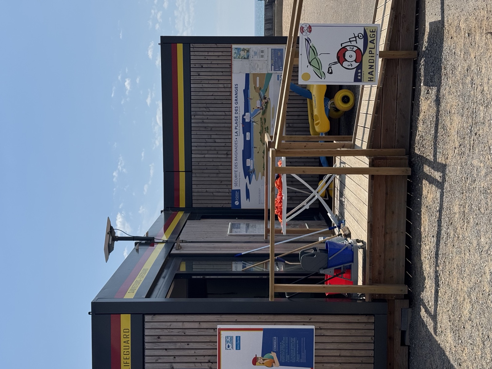 Le poste des Granges installé pour la saison : façade d'accueil, rampe bois, panneau Handiplage, tiralo jaune et matériel de secours sortis devant l'entrée