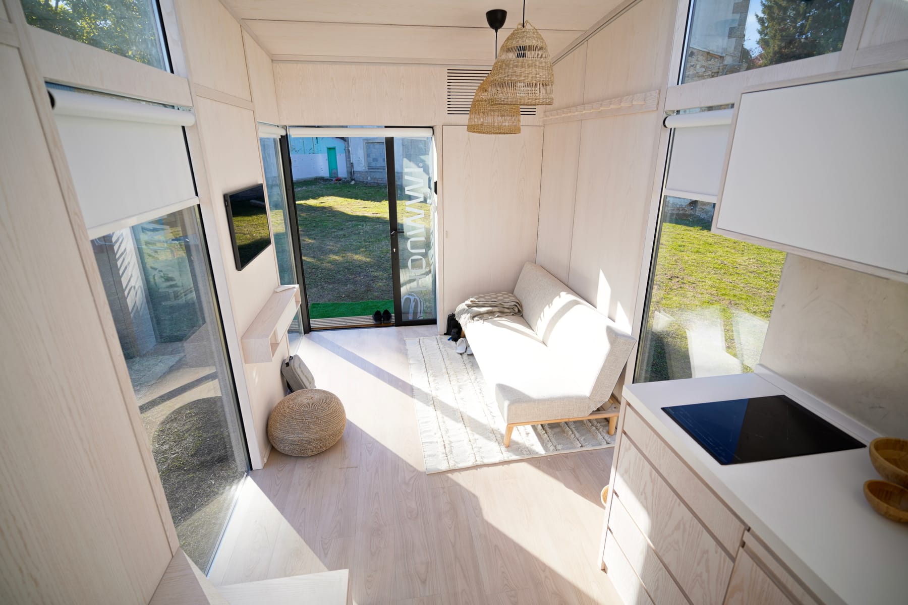 Pièce de vie d'un module Hoummi vue depuis la mezzanine : banquette face à la baie coulissante, cuisine à droite, sol et parois en bois clair